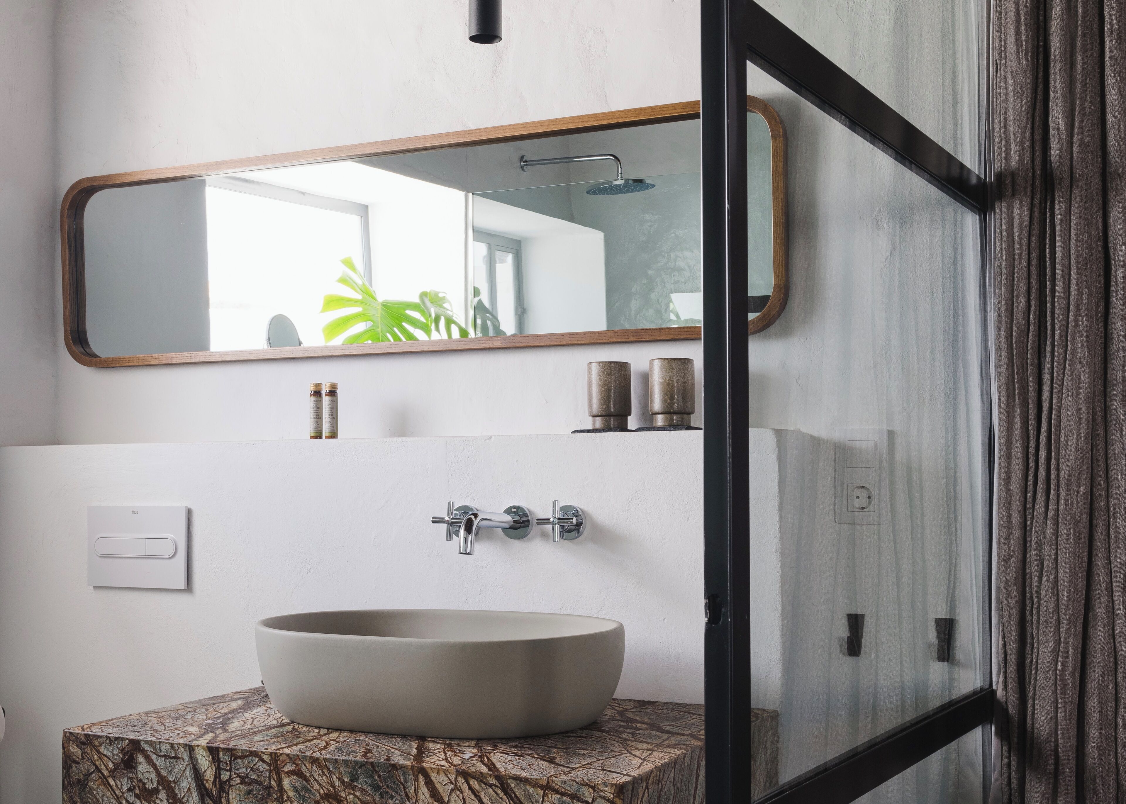 Une salle de bain dotée d’un grand lavabo ovale, d’un miroir avec un cadre en bois et d’un espace douche visible à travers une porte en verre.