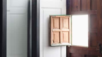 A corner of a room with a white door, a wooden window frame, and a wooden bench.
