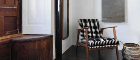 Une porte en bois, un mur blanc, une chaise à motifs noir et blanc, un panier tressé et un tableau abstrait gris.