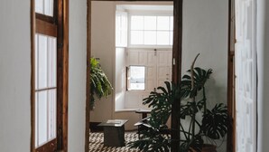 A narrow hallway with a wooden door frame, a potted plant, and a tiled floor leading to a room with a window and a door. - Casa de las Flores - Hotel Boutique Lanzarote (Teguise)