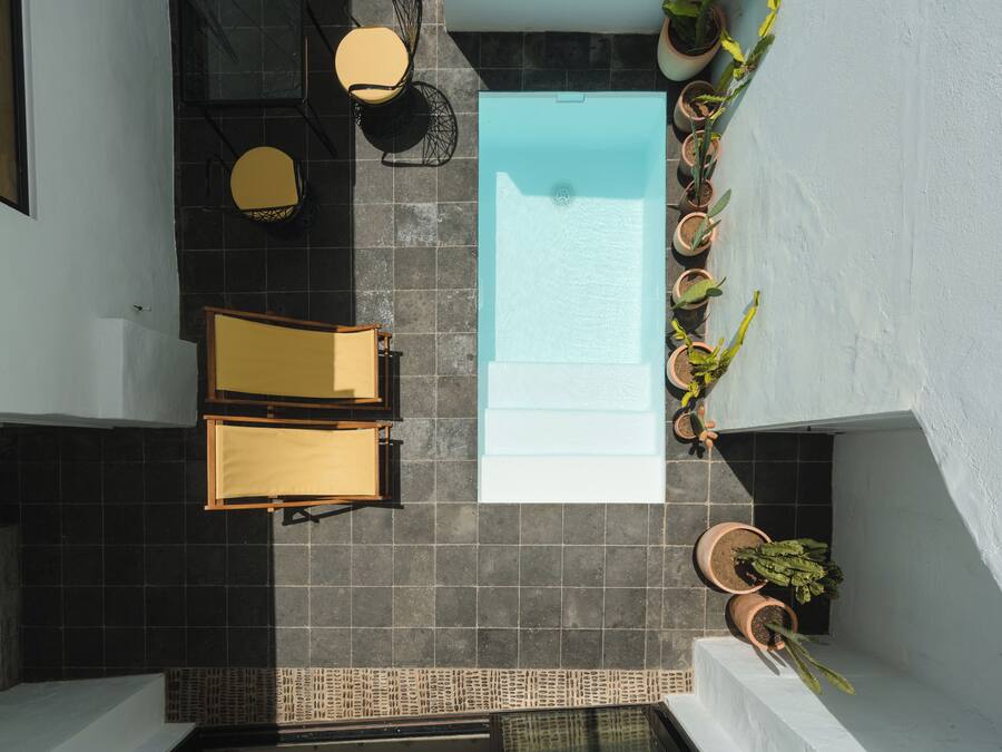 Una piscina en la azotea con dos sillas amarillas y una mesa, rodeada de plantas en macetas.