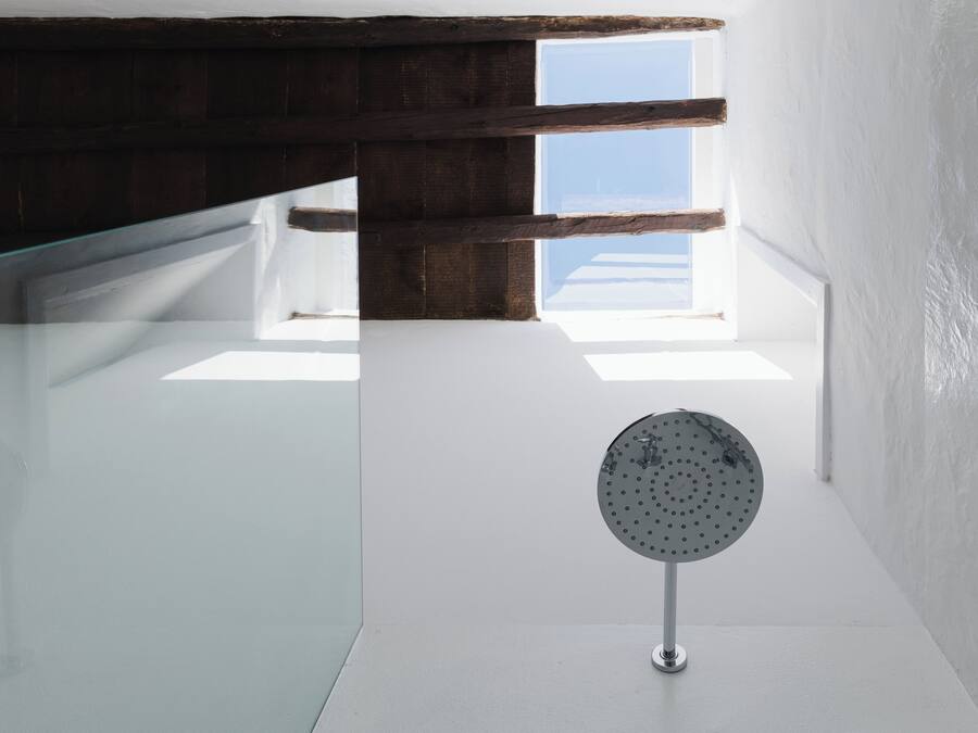 A modern bathroom with a glass shower enclosure, a round showerhead, and a view of the sky through a skylight.