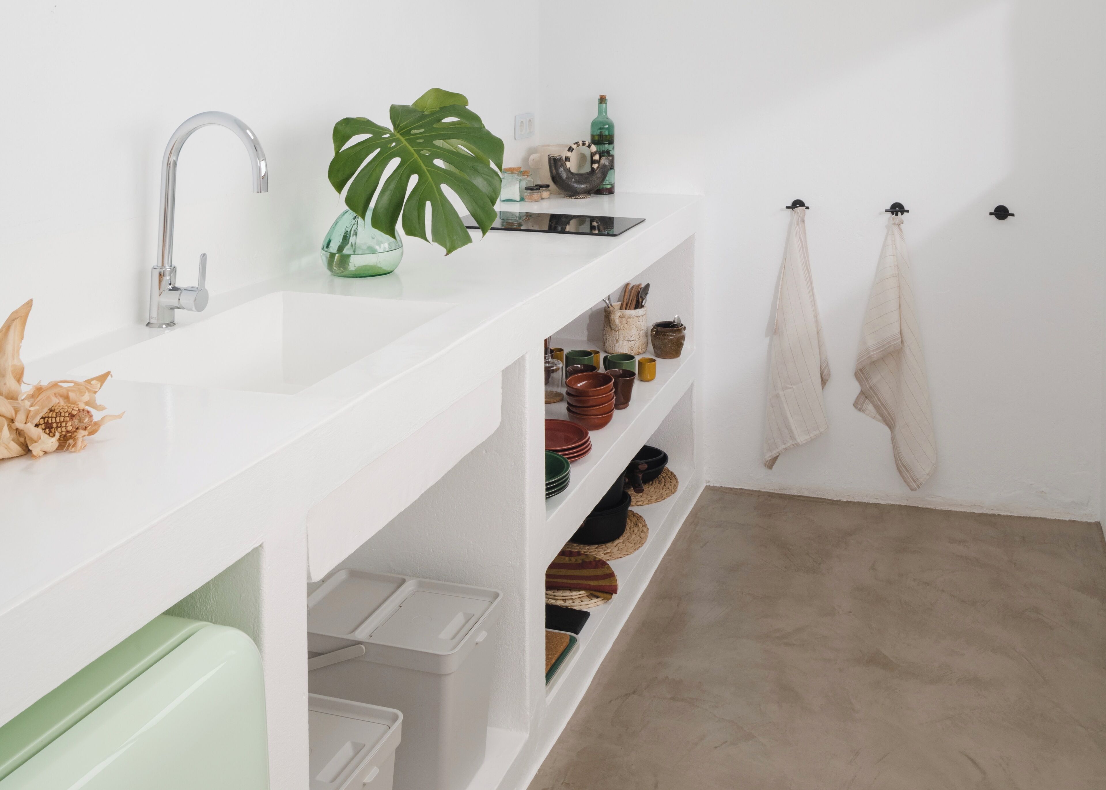 A white bathroom with a modern sink, shelves with dishes, and a plant.