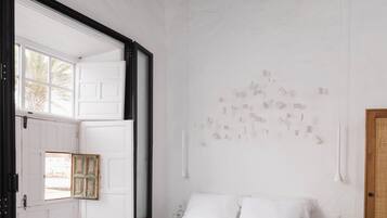 A minimalist bedroom with a large bed, a small bedside table, a nightstand, a window with a view, and a wall-mounted light fixture.