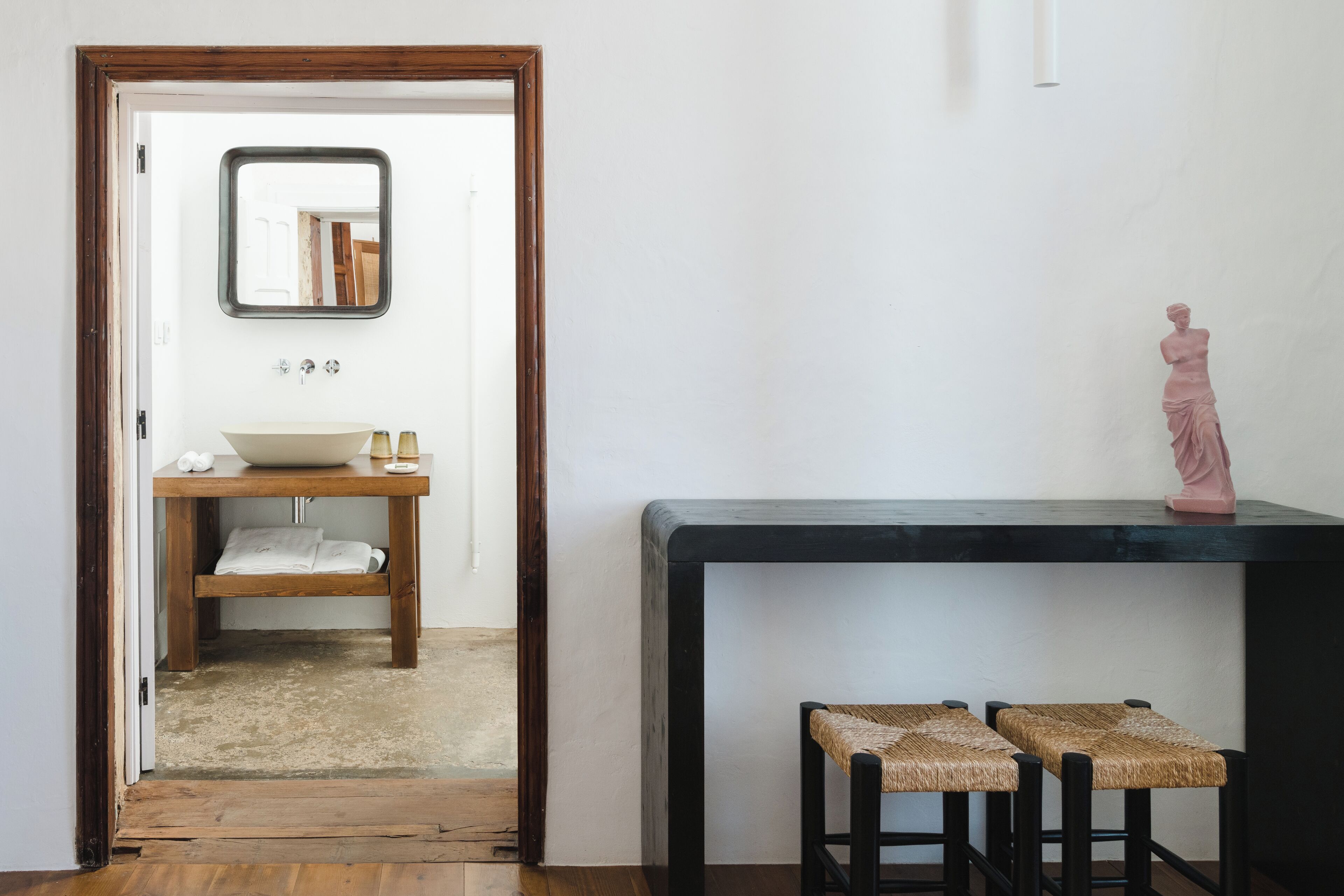 A bathroom with a wooden vanity, a sink, a mirror, and a statue on a console table.