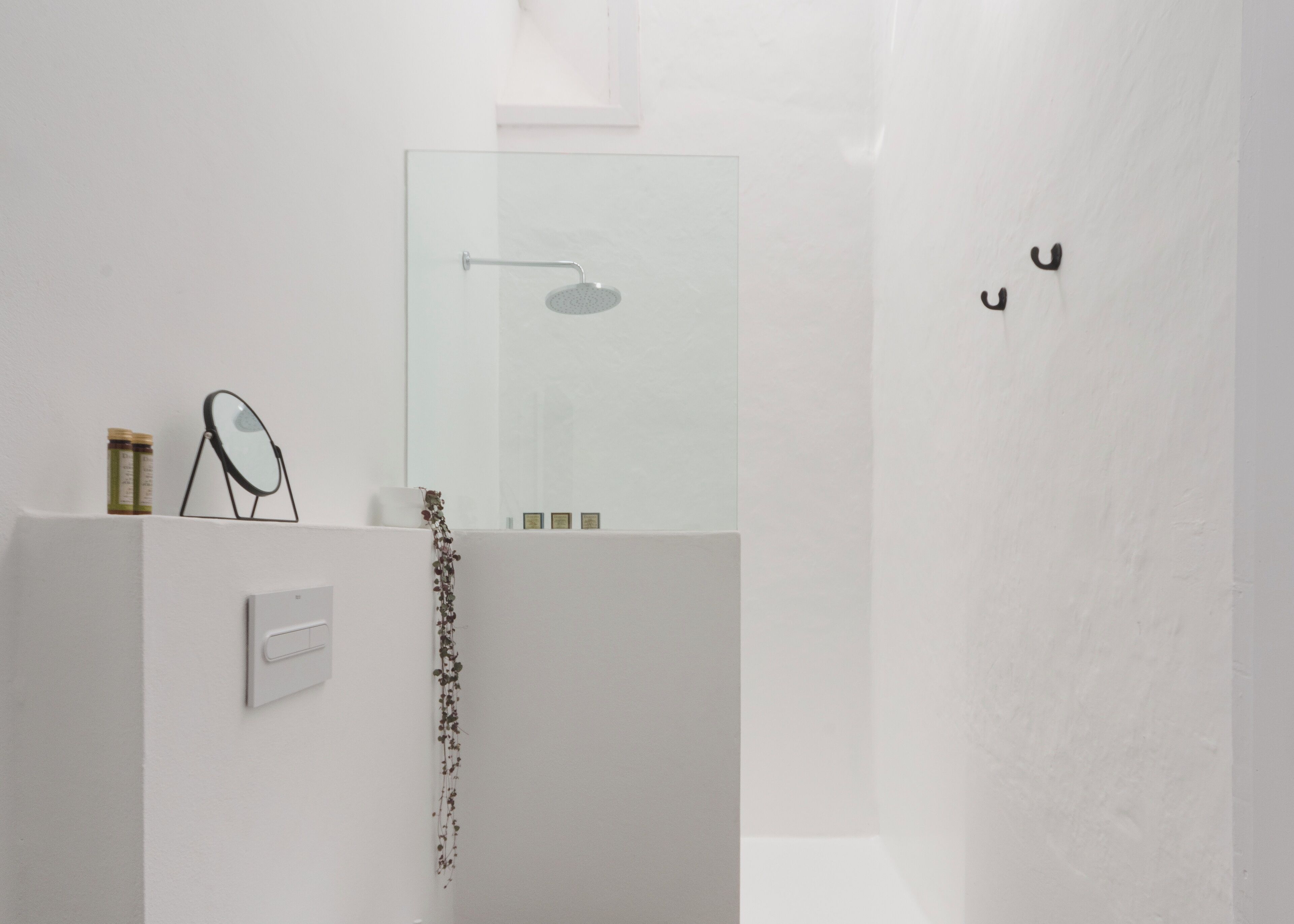 A modern bathroom with a glass shower enclosure, a small mirror, and a few toiletries on a shelf.