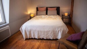 A bedroom with a large bed, two bedside tables with lamps, a window, and a wooden floor. - Gîte Prairie (Bergues)