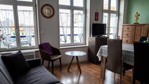 A living room with a sofa, chairs, a small round table, a TV, and a cabinet. - Gîte Prairie (Bergues)
