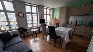A compact living space with a dining area, a sofa, a TV, and a kitchen. - Gîte Prairie (Bergues)