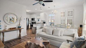 A modern living room with a sofa, coffee table, and a dining area with a chandelier. - Coconut Cottage 331–Spacious Condo–Sleeps 8 (Santa Rosa Beach)