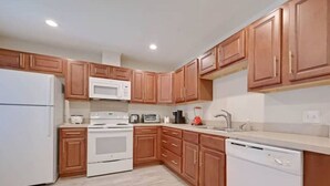 A modern kitchen with wooden cabinets, white appliances, and a light-colored floor.