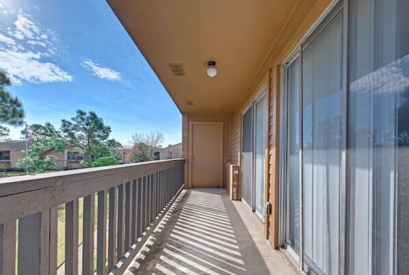 A balcony with a view of trees and buildings, a door, and a light fixture.