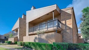 A modern two-story house with a balcony, a stone facade, and a well-maintained lawn.