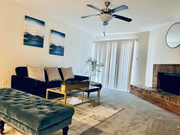 Relax in this stylish living room with a tufted sofa, matching ottoman, and coffee table, complemented by a large window and brick fireplace.