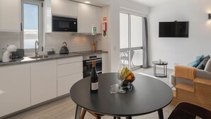 A modern kitchen with white cabinets, a black countertop, and a dining table with a bottle of wine and glasses. - Premium quiet apt, Funchal seafront | Oceanbreeze (Funchal)