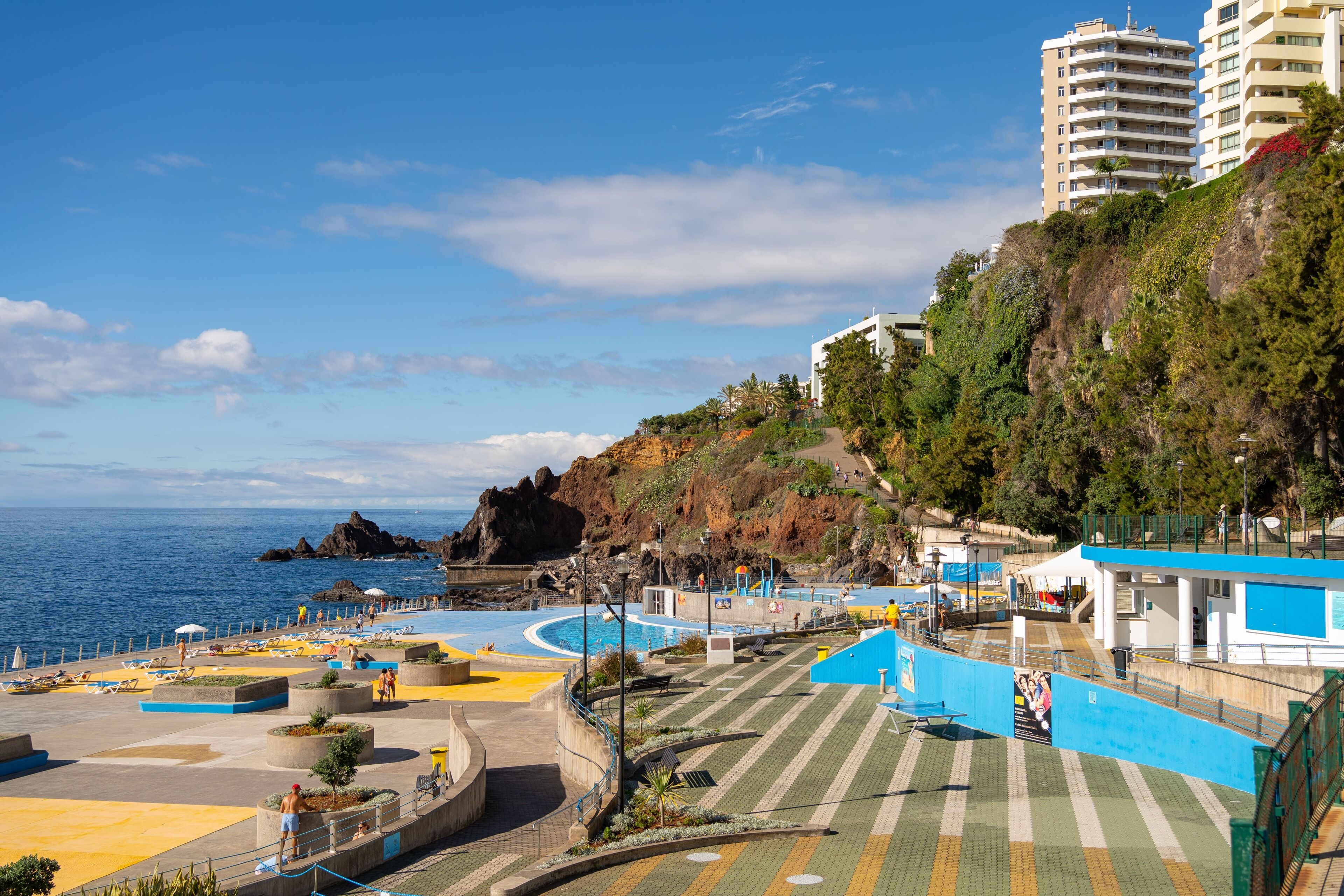 A coastal resort with a swimming pool, beach area, and buildings on a hillside.