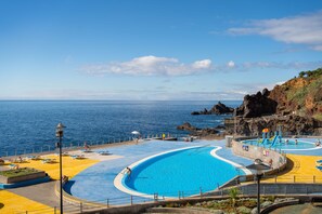 Une piscine en bord de mer, avec une eau d’un bleu limpide, entourée d’un paysage rocheux et offrant une vue sur la mer.
