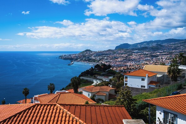 Un paysage urbain côtier avec des bâtiments aux toits de tuiles rouges, un ciel bleu dégagé et une vue sur la mer.