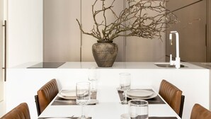 Un comedor moderno con una mesa blanca preparada para cuatro personas, rodeada de sillas de cuero marrón.