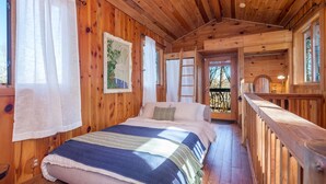 Une chambre dans une cabane en bois, avec un lit, une échelle et un balcon.