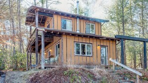 Une cabane en bois dotée d’une terrasse, de grandes fenêtres et d’une cheminée.