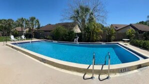A rectangular swimming pool with a ladder, surrounded by a concrete deck and palm trees. - Lovely 1 bedroom unit with pool (Sebring)