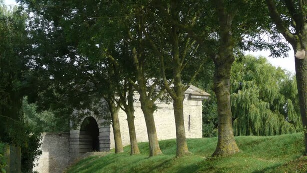 Un sendero lleva a un edificio de piedra con una entrada arqueada, rodeado de árboles y césped.