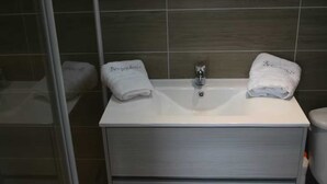 Un baño con un lavabo blanco, dos toallas con el texto 'Bergenshus', un box de ducha de cristal y un armario gris.