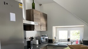 Una cocina moderna con un refrigerador de acero inoxidable, armarios de madera, un horno empotrado y una zona de comedor con una mesa y un banco de madera.