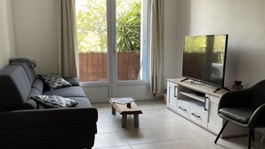 Una sala de estar con un sofá, una mesa de centro, un televisor sobre un mueble bajo y un ventanal con cortinas.