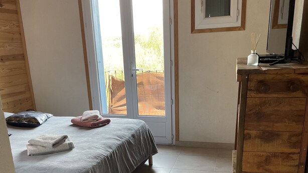 Un dormitorio con cama, cómoda, espejo y puerta corrediza de vidrio que da a un espacio exterior.