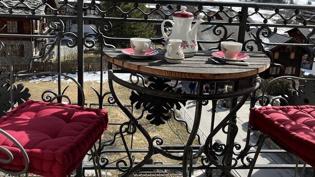 A balcony with a table set for tea, overlooking a snowy mountain village. - In Evolene, sunny studio with stunning view over the mountains (Evolène)