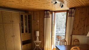 A cozy wooden cabin interior with a dining area, a fluffy chair, a small table, and a cabinet with glass doors. - In Evolene, sunny studio with stunning view over the mountains (Evolène)