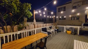 Un espace extérieur aménagé en terrasse, avec un sol en bois, une balustrade blanche et des guirlandes lumineuses.