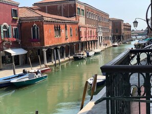 A canal with boats, historic buildings, and a bridge. - Vetrai House – View of the Canal in Murano – Venice (Venezia)
