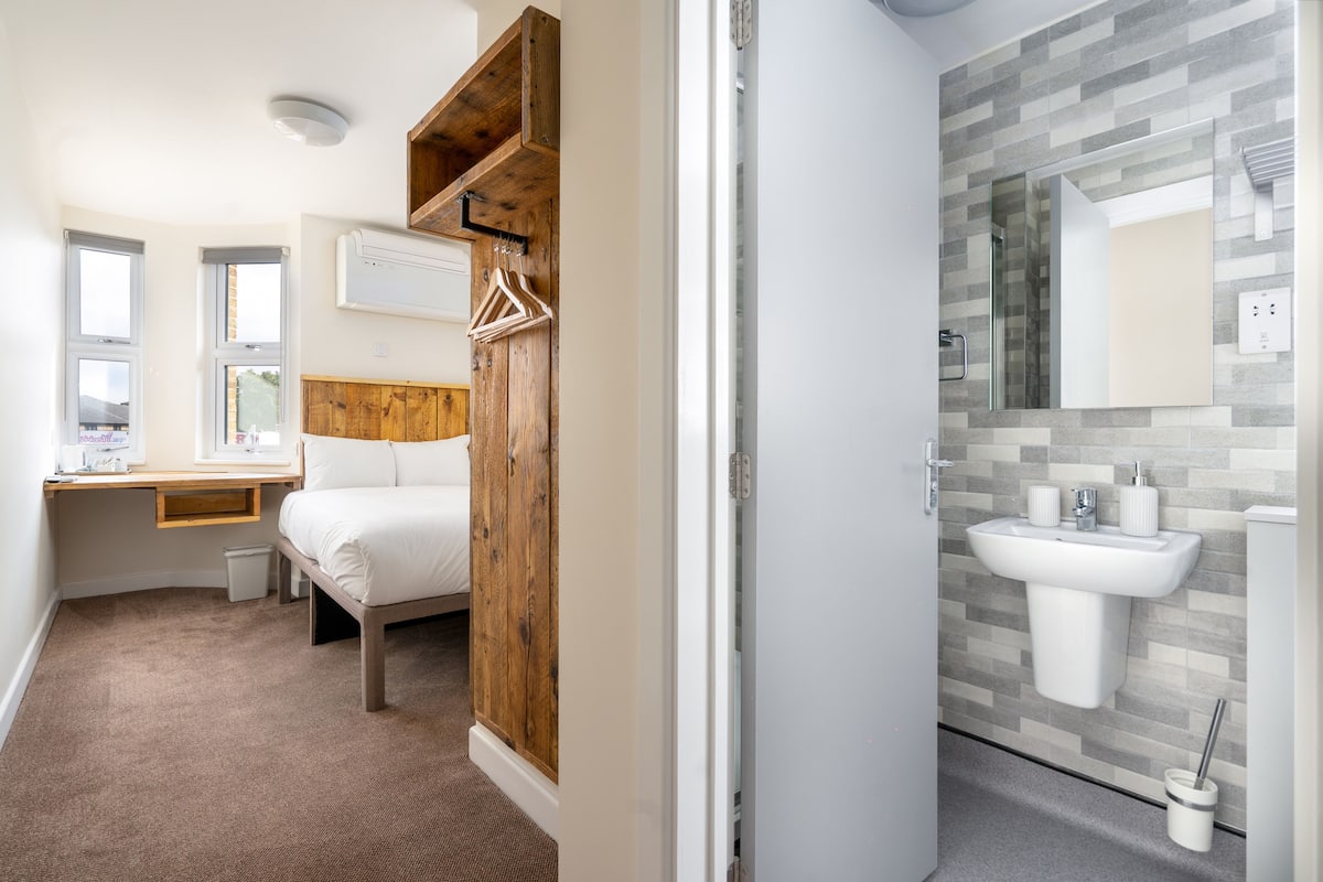 A bedroom with a bed, wooden wardrobe, bedside table, and a window.