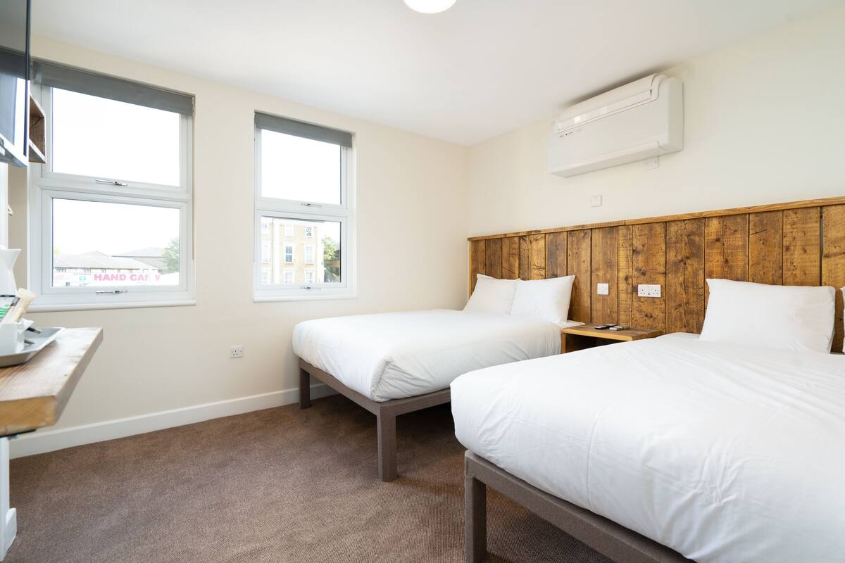 A hotel room with two beds, a wooden headboard, a desk with a lamp, and a window.
