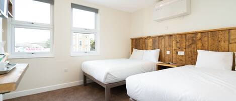 A hotel room with two beds, a wooden headboard, a desk with a lamp, and a window.