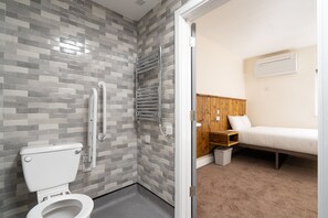 A bathroom with a toilet, grab bars, and a shower area.