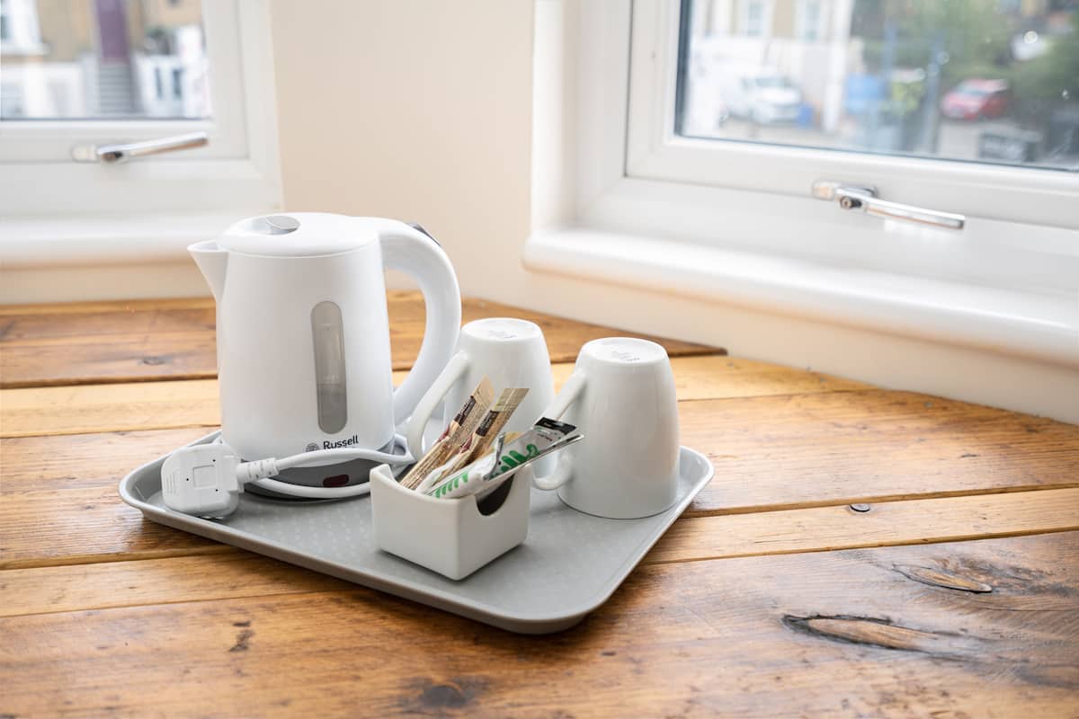 A tray with a white electric kettle, a mug, and a cup on a wooden table near a window.