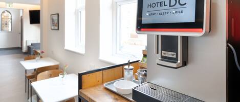 Zona de recepción de un hotel con un panel digital que muestra “HOTEL DC” y el lema “DESCANSAR . DORMIR . SONREÍR”.