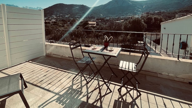 Een balkon met een tafel en stoelen, met uitzicht op een bergachtig landschap.