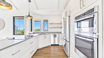 Une cuisine moderne avec des meubles blancs, des appareils électroménagers en acier inoxydable et un plancher en bois.