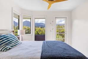Quarto com cama, mesa de cabeceira, abajur e vista para montanhas através de uma porta.