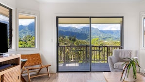 Een balkon met uitzicht op bergen, een televisie, een houten stoel, een bank en een bloempot met plant.