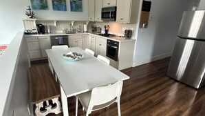 A modern kitchen with white cabinetry, a stainless steel refrigerator, and a dining area with a white table and chairs. - Lakeside three bedroom boathouse. (Wasilla)