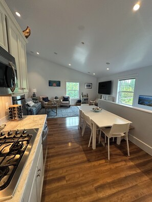 A modern kitchen with a dining area, wooden flooring, and a large window.