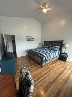 A bedroom with a wooden bed, a ceiling fan, a painting on the wall, and a desk with a chair.