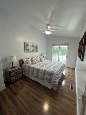A bedroom with a bed, nightstand, ceiling fan, window, and artwork on the wall. - Lakeside three bedroom boathouse. (Wasilla)