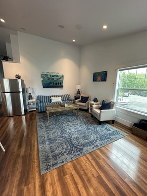 A modern living room with a blue patterned rug, a striped sofa, a beige armchair, a coffee table, and a refrigerator.